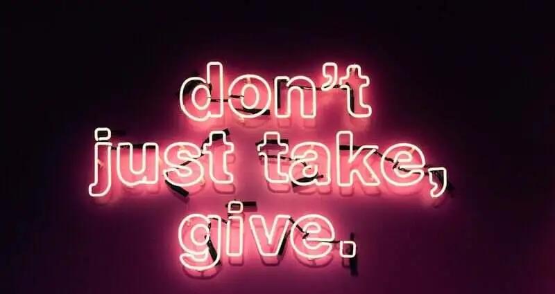 Neonlicht mit der Botschaft 'don't just take, give.' in pinker Schrift auf dunklem Hintergrund.