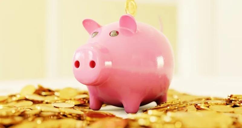 Rosa Sparschwein steht auf einem Haufen von goldenen Münzen.