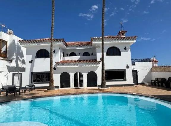 Villa mit einem Pool und Palmen in Gran Canaria unter blauem Himmel.