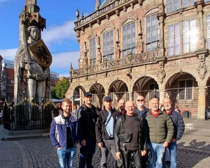 Eine Gruppe von sieben Personen posiert vor einem historischen Gebäude mit einer Statue in Bremen.