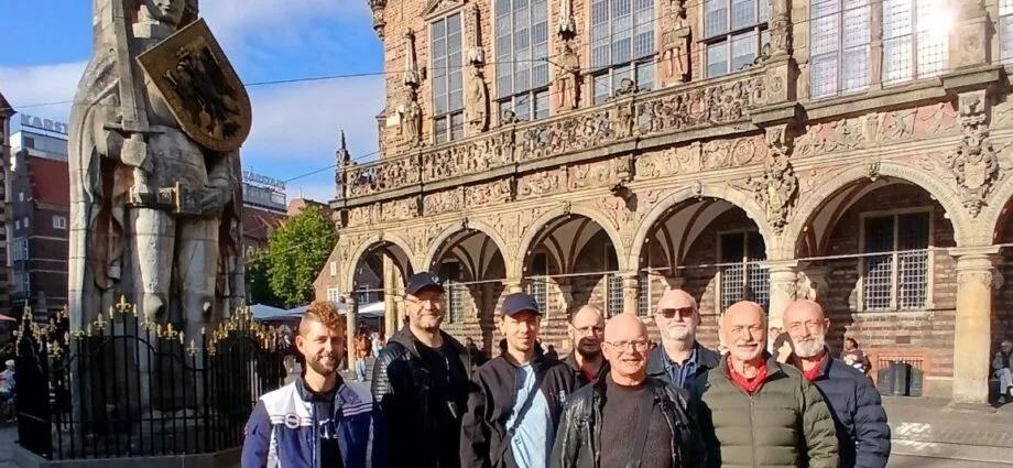 Eine Gruppe von sieben Personen posiert vor einem historischen Gebäude mit einer Statue in Bremen.